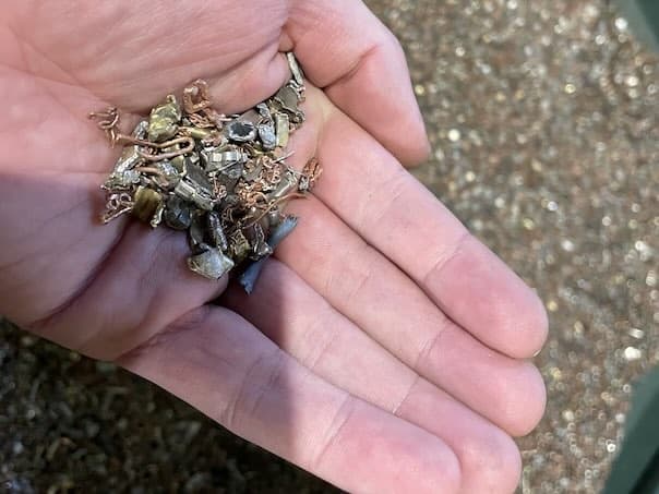 An open hand holding recovered metal fragments such as brass and copper from dismantled e-waste