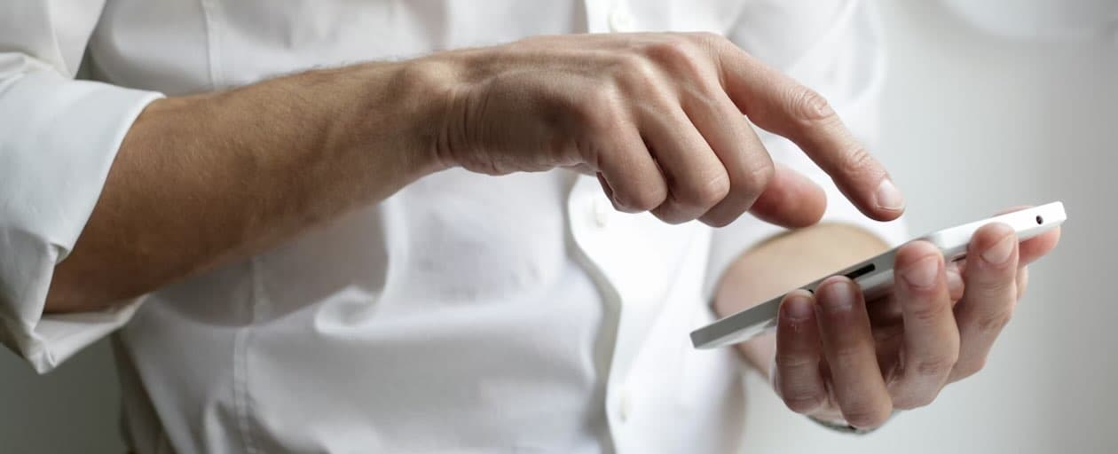 Close-up photo of a man's arms and hands, using their index finger to use a smartphone