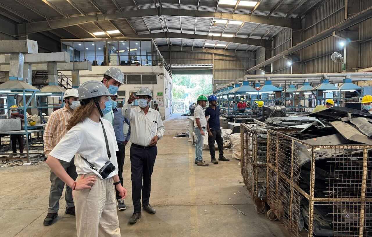 A group of business-casual professionals wearing helmets visit a recycling facility and look at dismantled devices