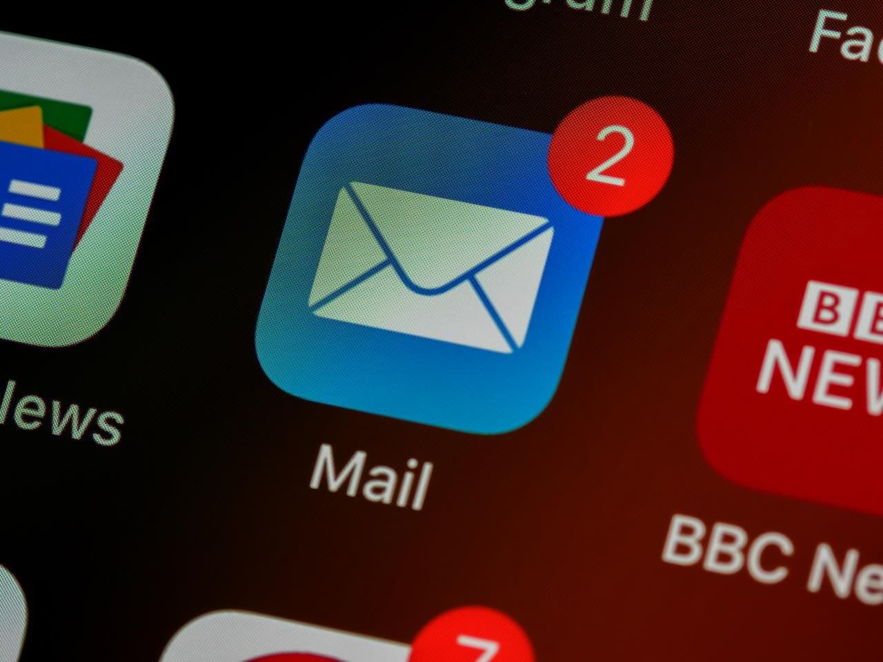 A close-up shot on an iPhone app overview screen with the Mail app icon centered and showing 2 unread emails