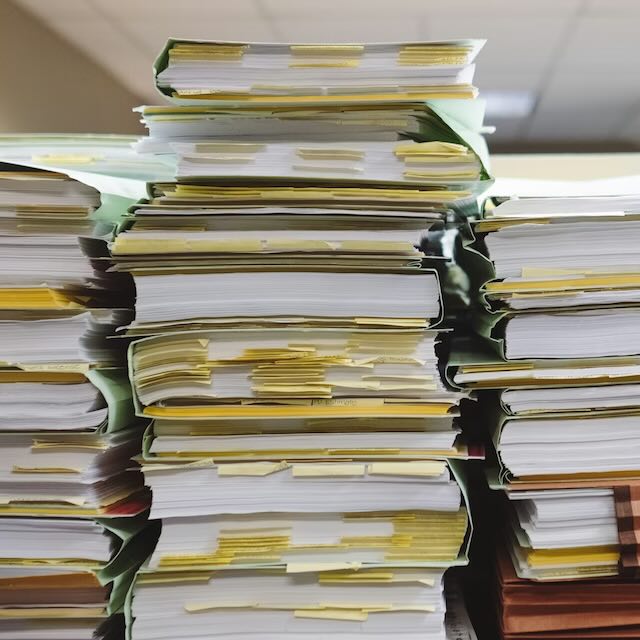 High stacks of paper files and documents organized with numerous yellow tabs and sticky notes