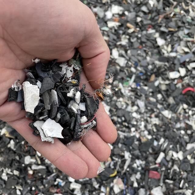 Hand holding a mixture of shredded electronic waste materials, including black plastic fragments and copper wire coils