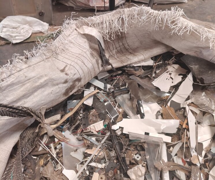 A close-up photo of an open industrial bag of e-waste, containing pieces of metal and plastic