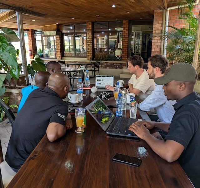 A group of Minimise and partner team members gather on a table to discuss something shown on a laptop